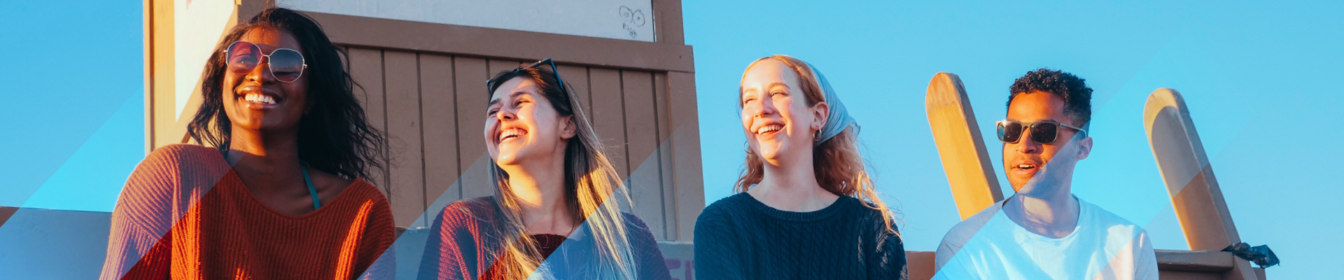 Four friends sat smiling on a wall with blue sky behind